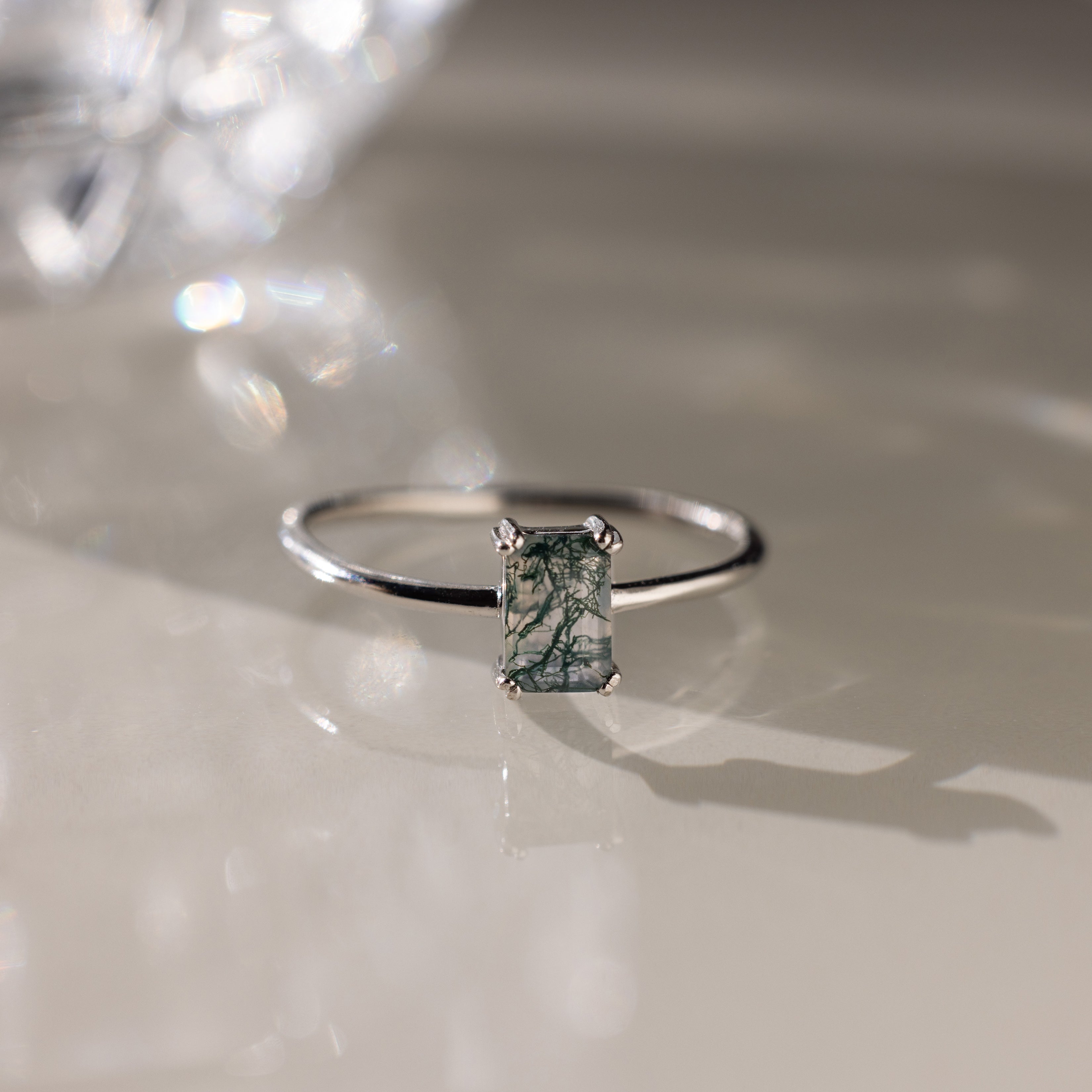 Silver ring with a green agate baguette-cut gemstone on a reflective surface