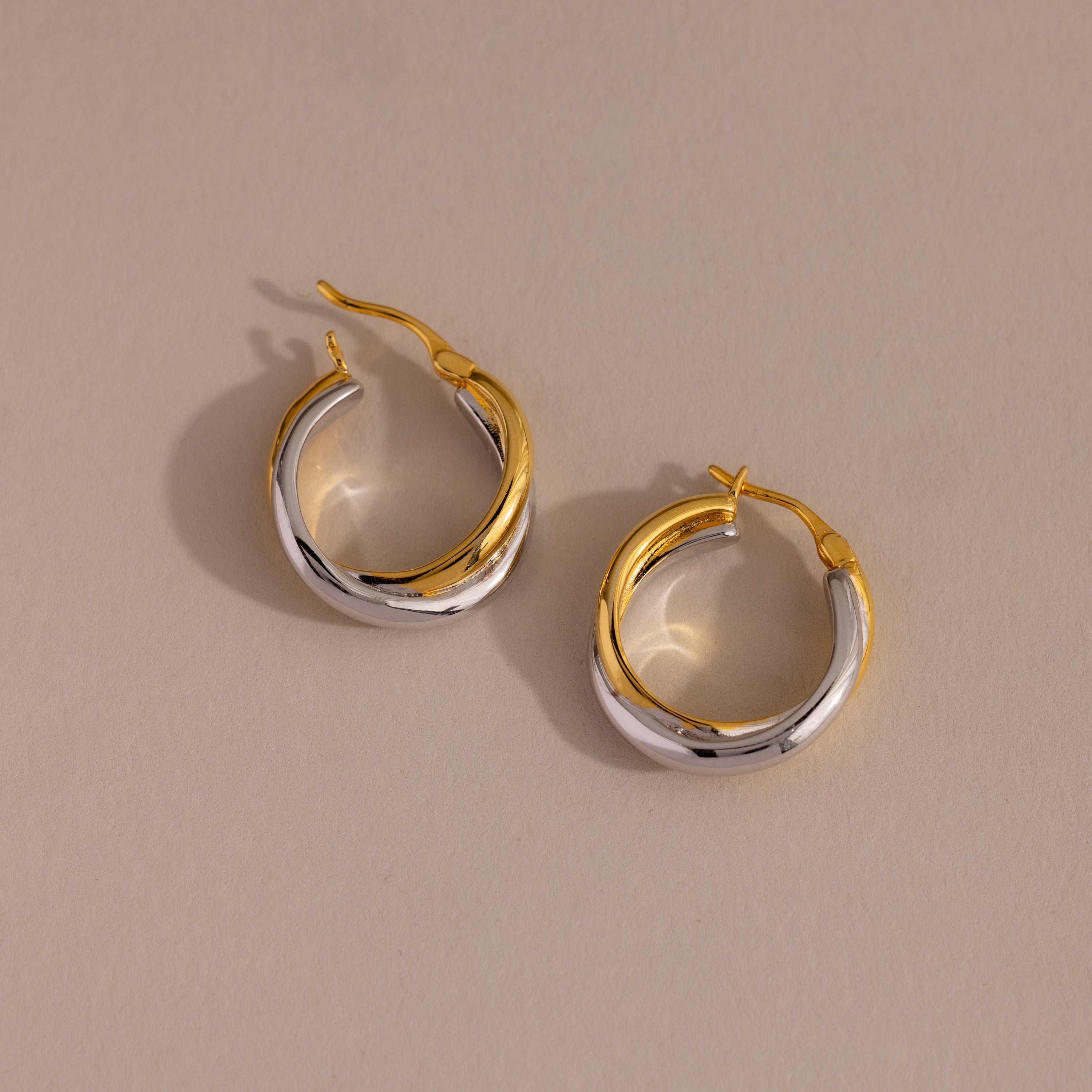 Twisted Mixed Metal Hoops—modern gold and silver twisted hoops—are elegantly displayed on a beige background.