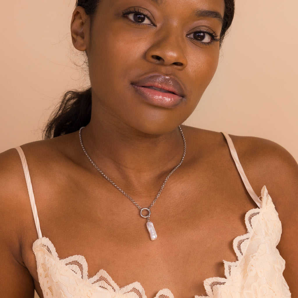 Woman in a cream lace top wears the Long Baroque Pearl Charm in Sterling Silver, highlighting its versatile style against a beige background.