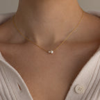 A close-up of a woman wearing the Dainty Duo Pearl Necklace, featuring two small pearls, styled with a cream sweater.