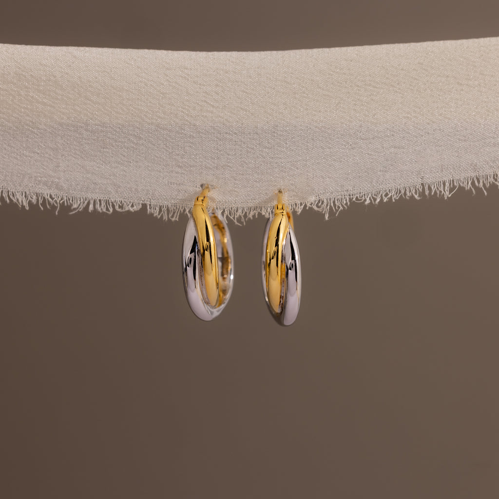 Twisted Mixed Metal Hoops—modern earrings with gold and silver twisted hoops—hang elegantly on white fabric against a plain background.