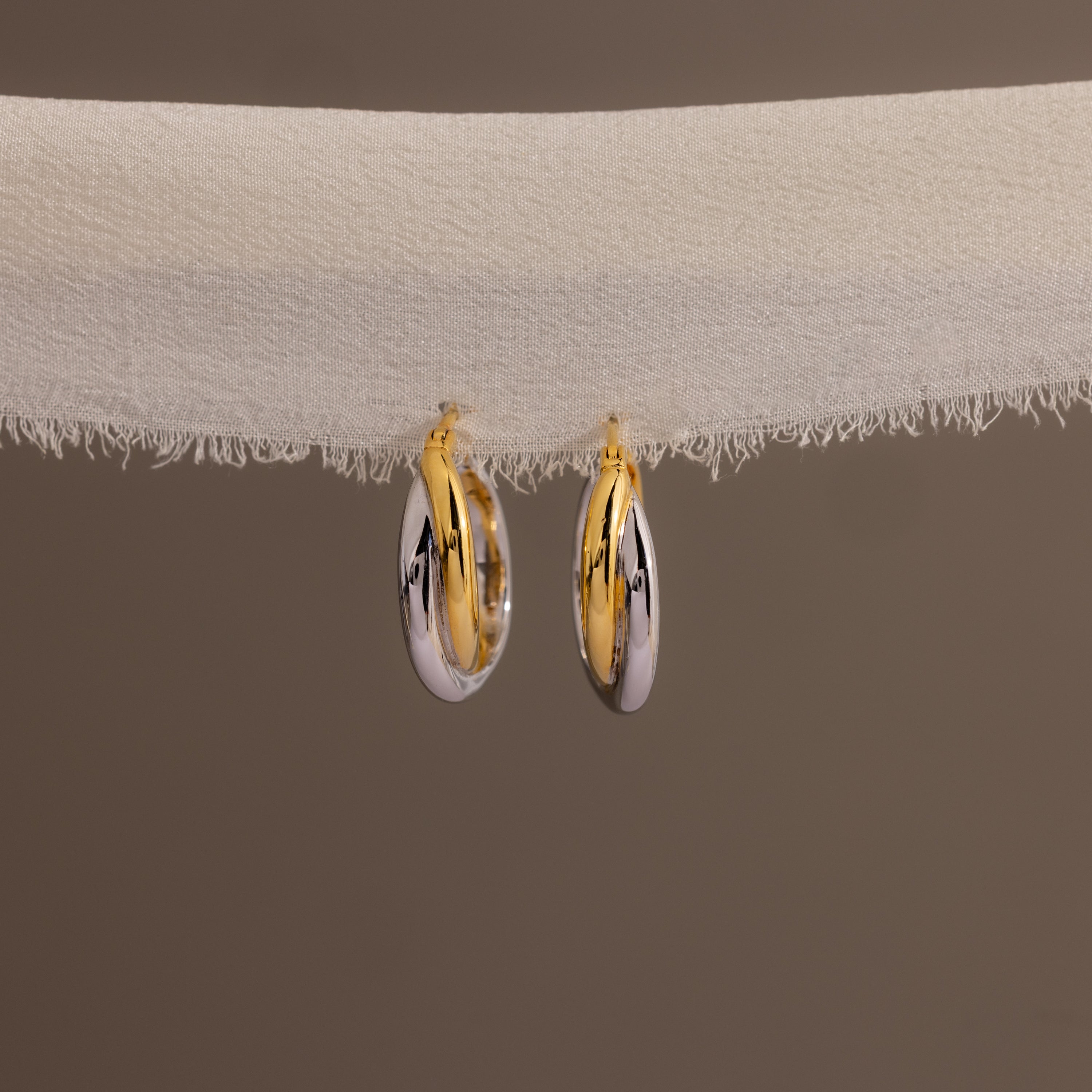 Twisted Mixed Metal Hoops—modern earrings with gold and silver twisted hoops—hang elegantly on white fabric against a plain background.
