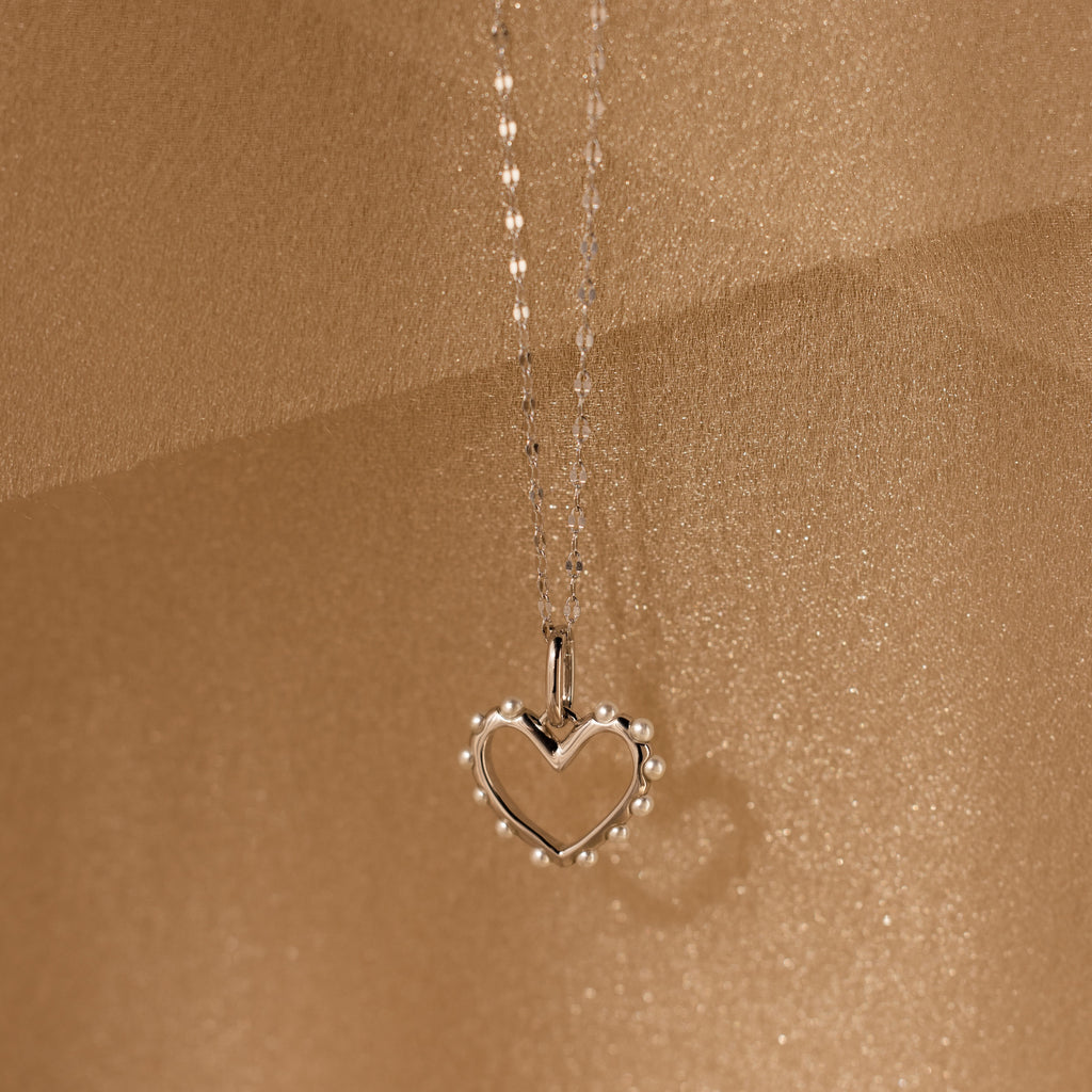 Classic Pearl Heart Charm in Sterling Silver necklace with a heart pendant and delicate pearl beads, beautifully showcased on a shimmering beige background.