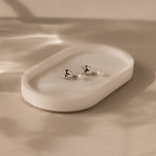 Heart Pearl Drop Earrings featuring delicate pearls in a heart shape rest on a white oval dish, softly lit by natural light—ideal for any occasion.