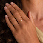 A hand with manicured nails wears the Birthstone Half Chain Ring, featuring a delicate gold band and a small gemstone on the ring finger—ideal for fans of dainty jewelry.