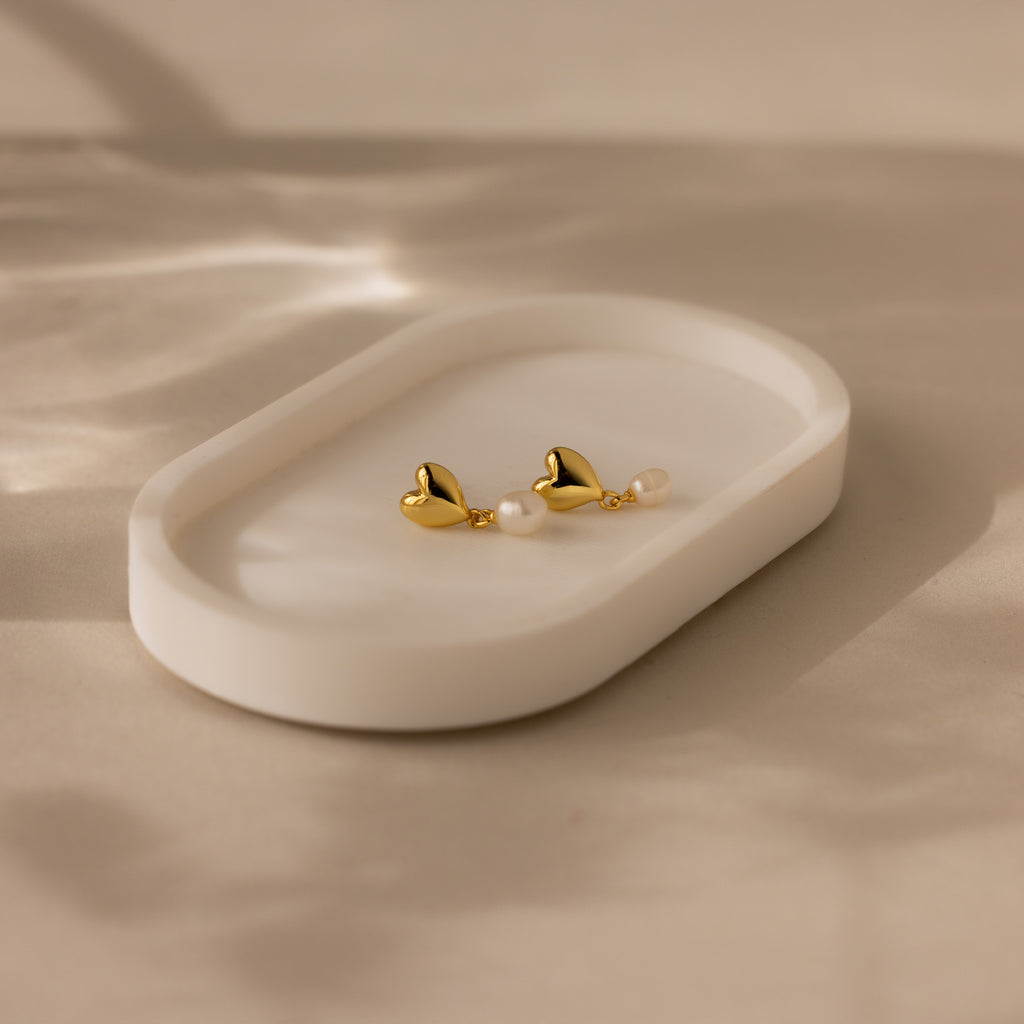 Heart Pearl Drop Earrings in 18K Gold with pearls are displayed on a white oval dish set against a soft beige background.
