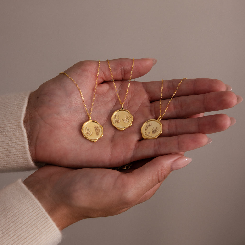 A hand holds three Baby Hand & Footprint Necklaces with engraved handprint pendants on delicate chains—perfect personalized jewelry for treasuring your little one's precious memories.
