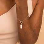 A person wears the Long Baroque Pearl Charm in Sterling Silver, a versatile chain bracelet featuring a dangling pearl that effortlessly complements any style.