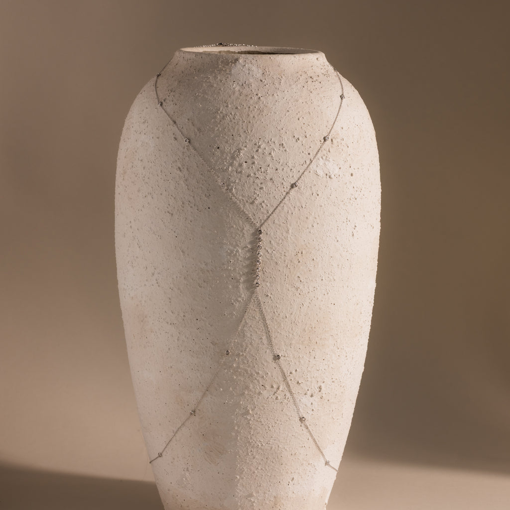 Close-up of the silver Sprinkle Diamond Body Chain displayed on a white ceramic vase, showing the full Y-shaped design and sparkling bezel-set stones.