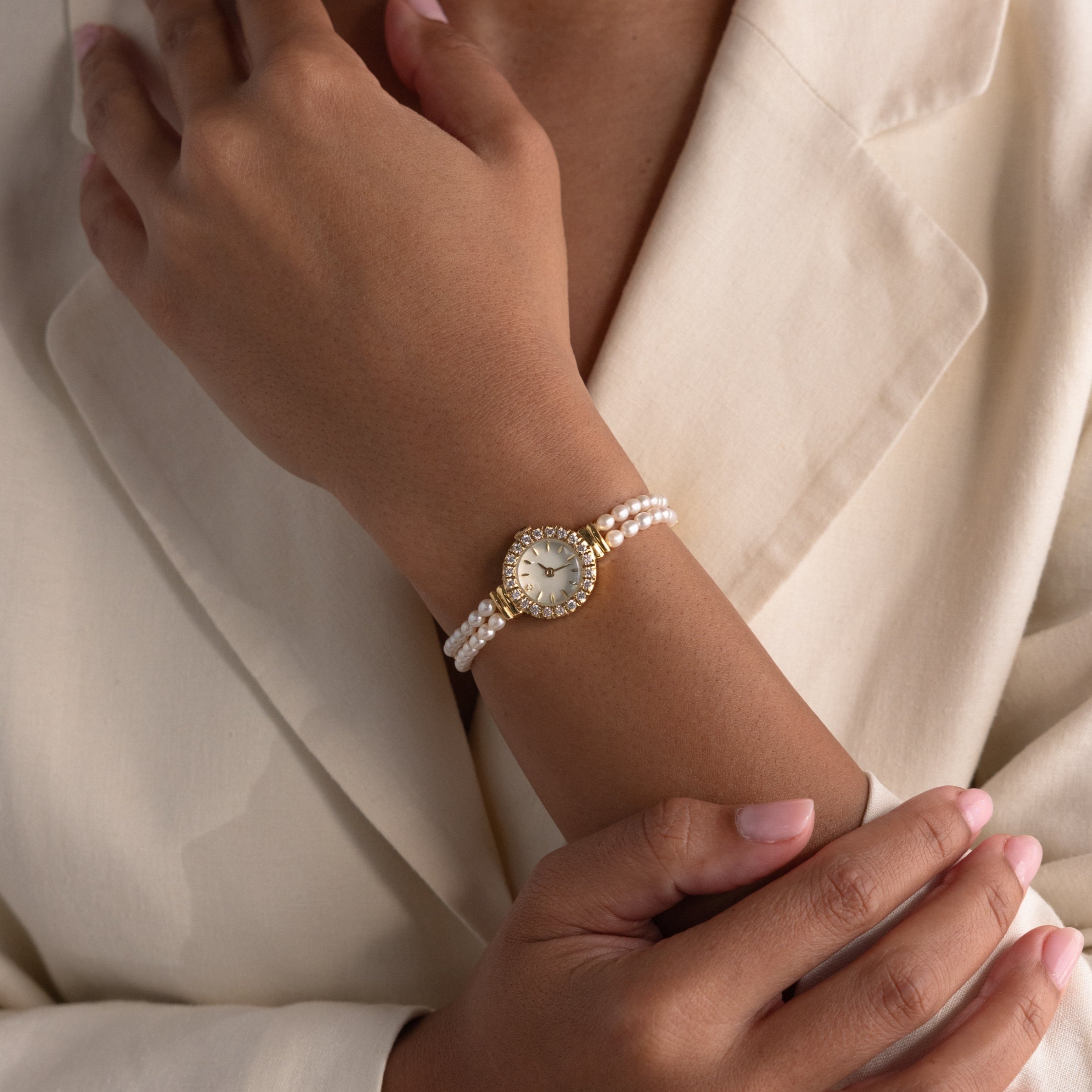 Someone wearing the Pearl Link Timepiece, featuring diamond accents and a gold bezel, paired with a cream blazer—showcasing vintage elegance.