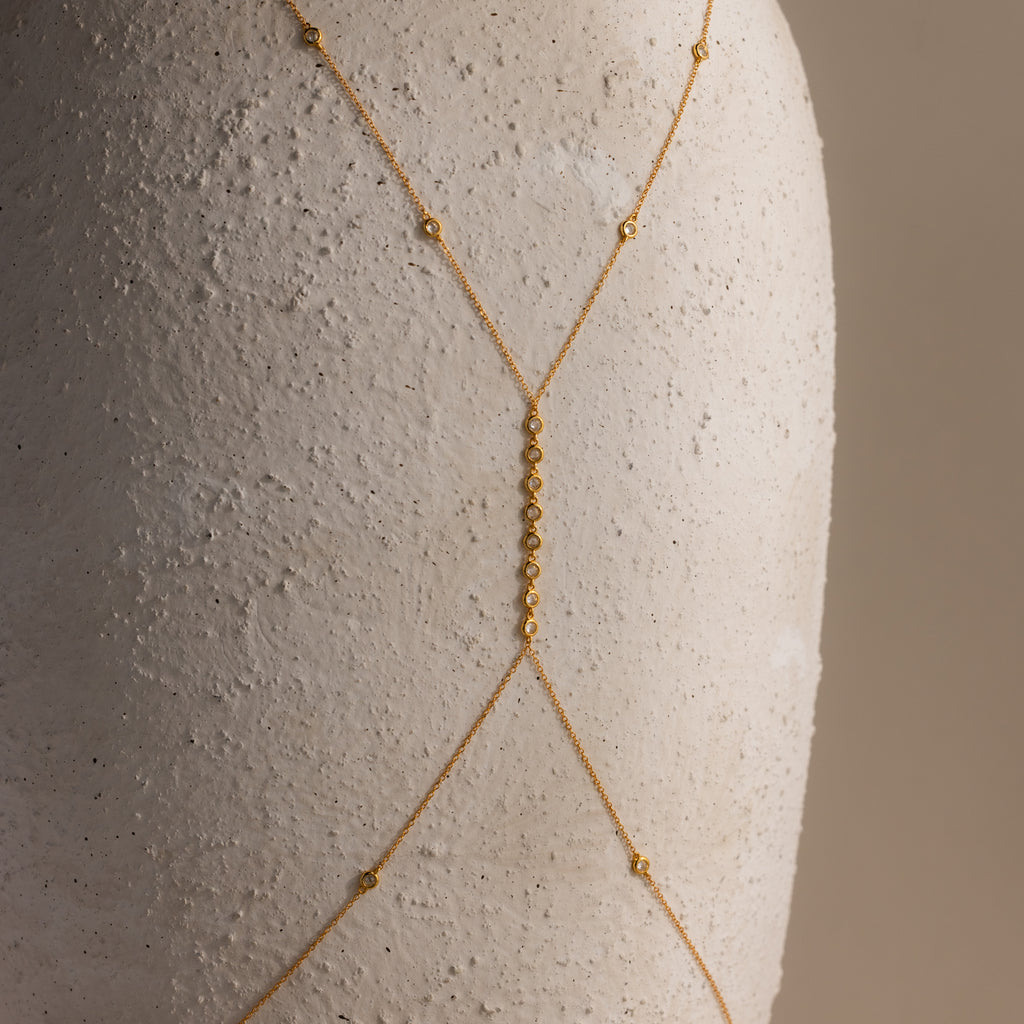 Macro shot of the gold Sprinkle Diamond Body Chain on textured white ceramic, highlighting the central vertical row of bezel-set diamonds and the fine gold chain.