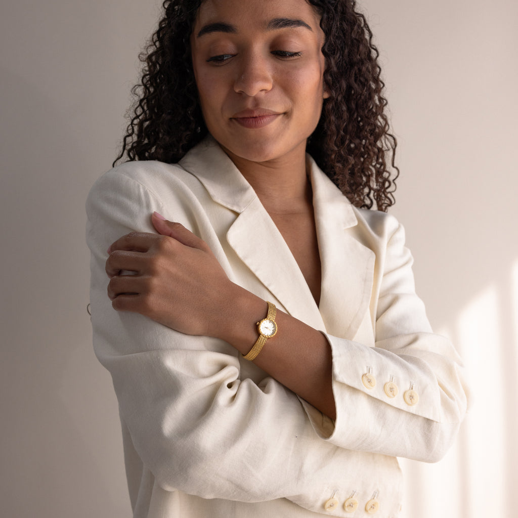 Woman in a cream blazer posing with arms crossed, wearing the round braided gold watch.