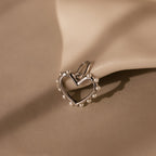 A Classic Pearl Heart Charm in Sterling Silver, adorned with pearl bead accents, rests on a smooth beige surface, evoking timeless elegance.