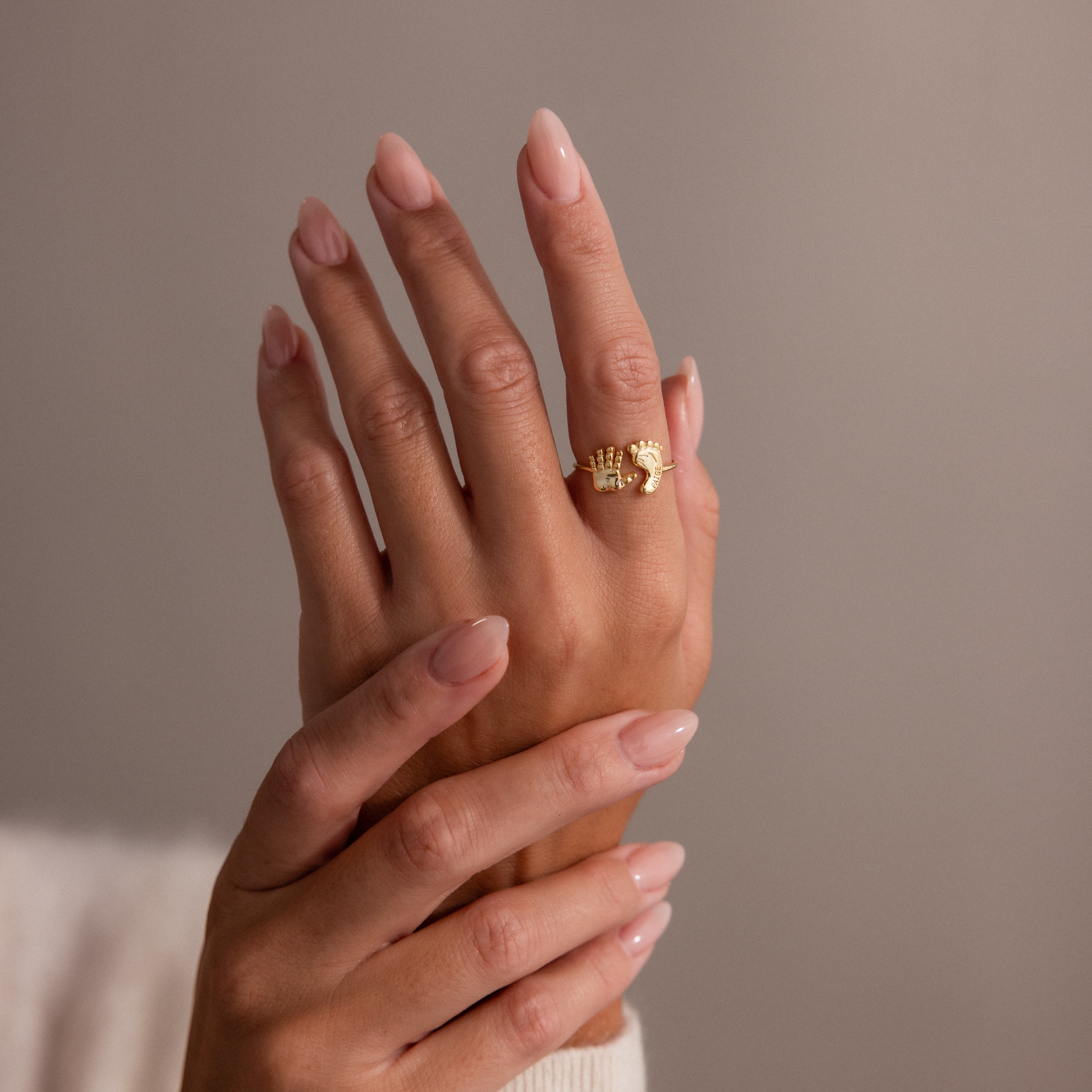 Two hands with manicured nails, one wearing the Hand & Footprint Duo Name Ring in Rose Gold on the index finger—a stunning piece of personalized keepsake jewelry.