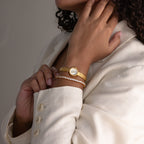 Close-up of the round braided gold watch stacked with a rhinestone tennis bracelet on a woman’s wrist.