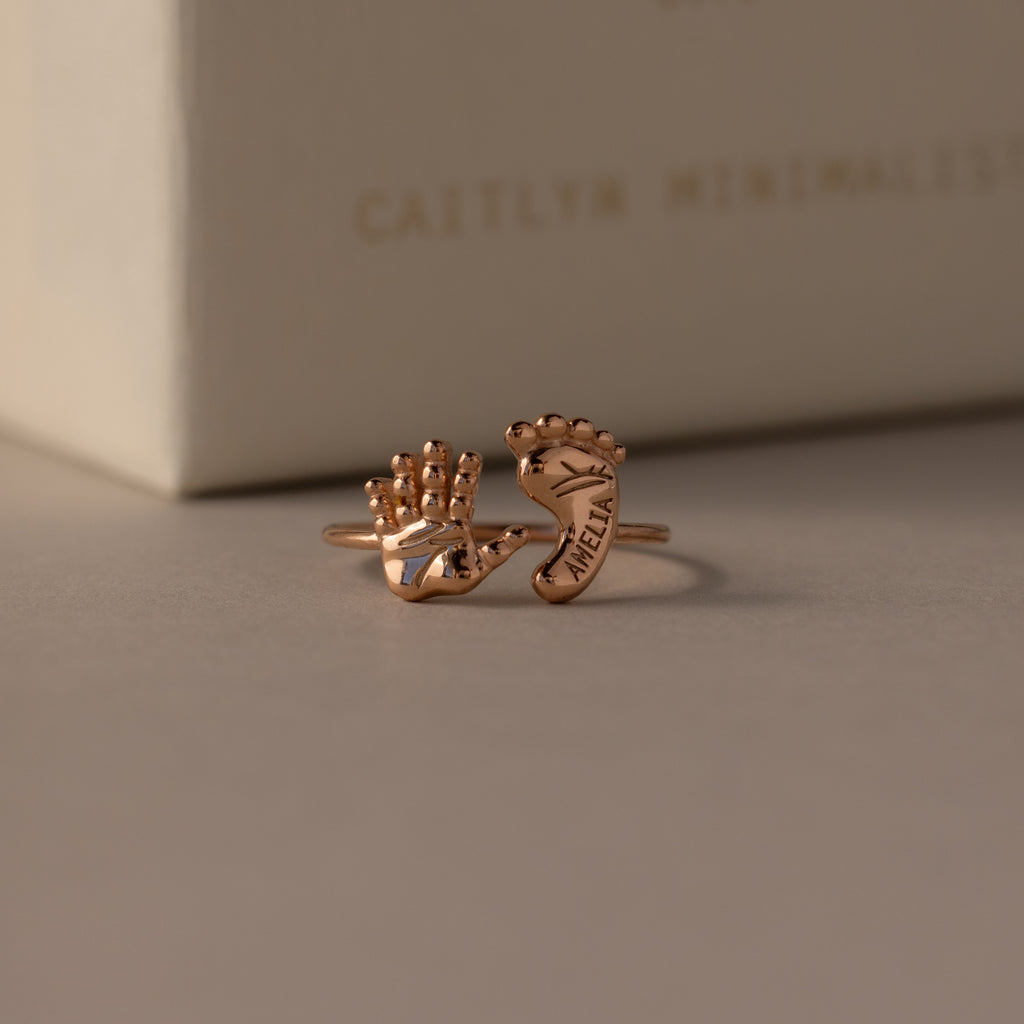 The Hand & Footprint Duo Name Ring in Rose Gold features delicate hand and foot shapes, engraved with a name for a personalized touch—an ideal keepsake jewelry gift for new parents.