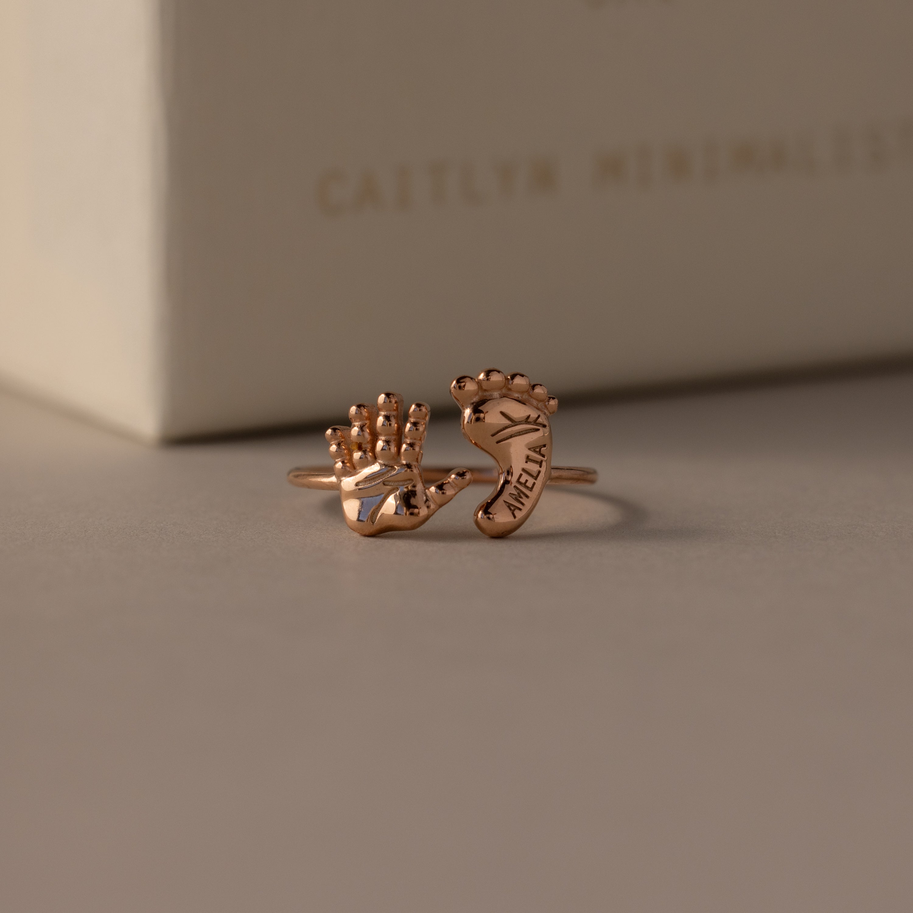 The Hand & Footprint Duo Name Ring in Rose Gold features delicate hand and foot shapes, engraved with a name for a personalized touch—an ideal keepsake jewelry gift for new parents.