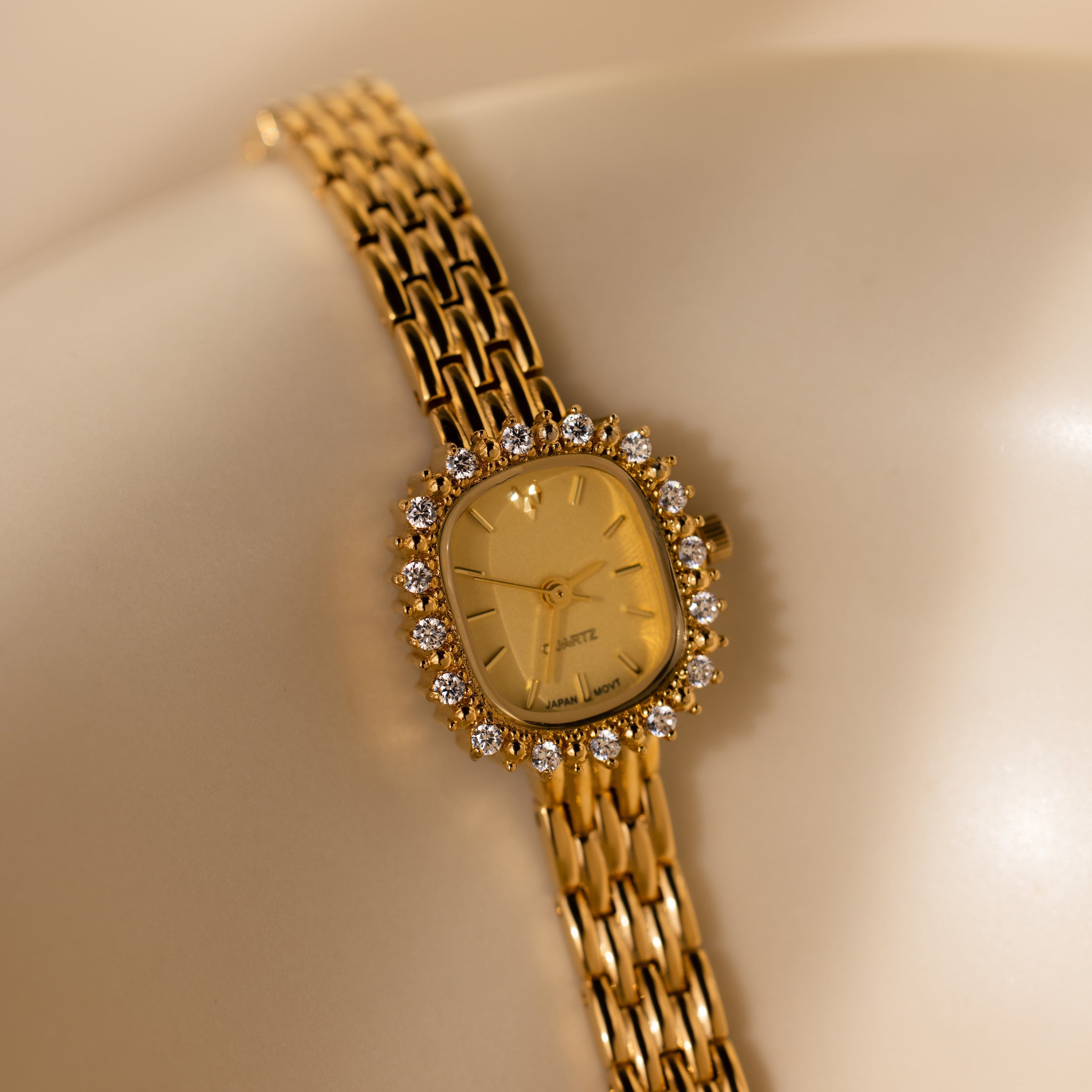 The Pave Blossom Timepiece in Diamond features a diamond-studded bezel and linked bracelet, radiating elegance as it shines on a smooth, neutral surface.