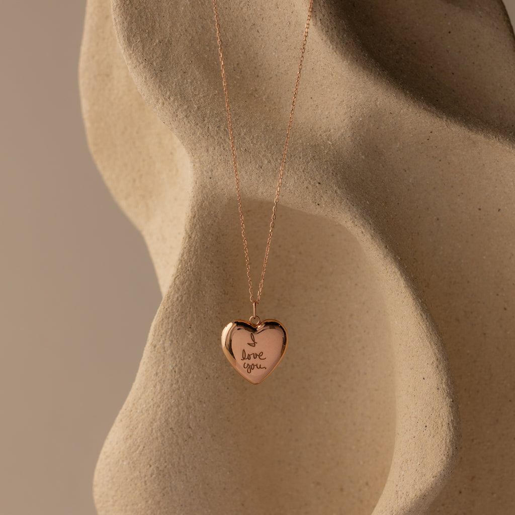 Flatlay of our Handwriting Heart Locket Necklace in Rose Gold with the words "I love you" engraved
