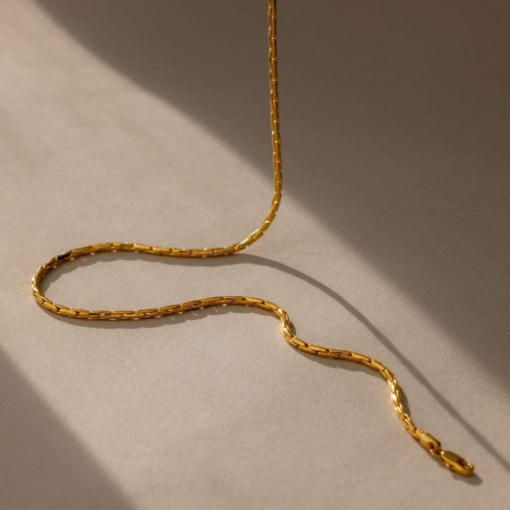 The Bold Link Chain Necklace in 18K Gold rests in gentle curves on a beige surface, casting soft, angled shadows—an eye-catching modern chain made to stand out.