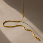 The Bold Link Chain Necklace in 18K Gold rests in gentle curves on a beige surface, casting soft, angled shadows—an eye-catching modern chain made to stand out.