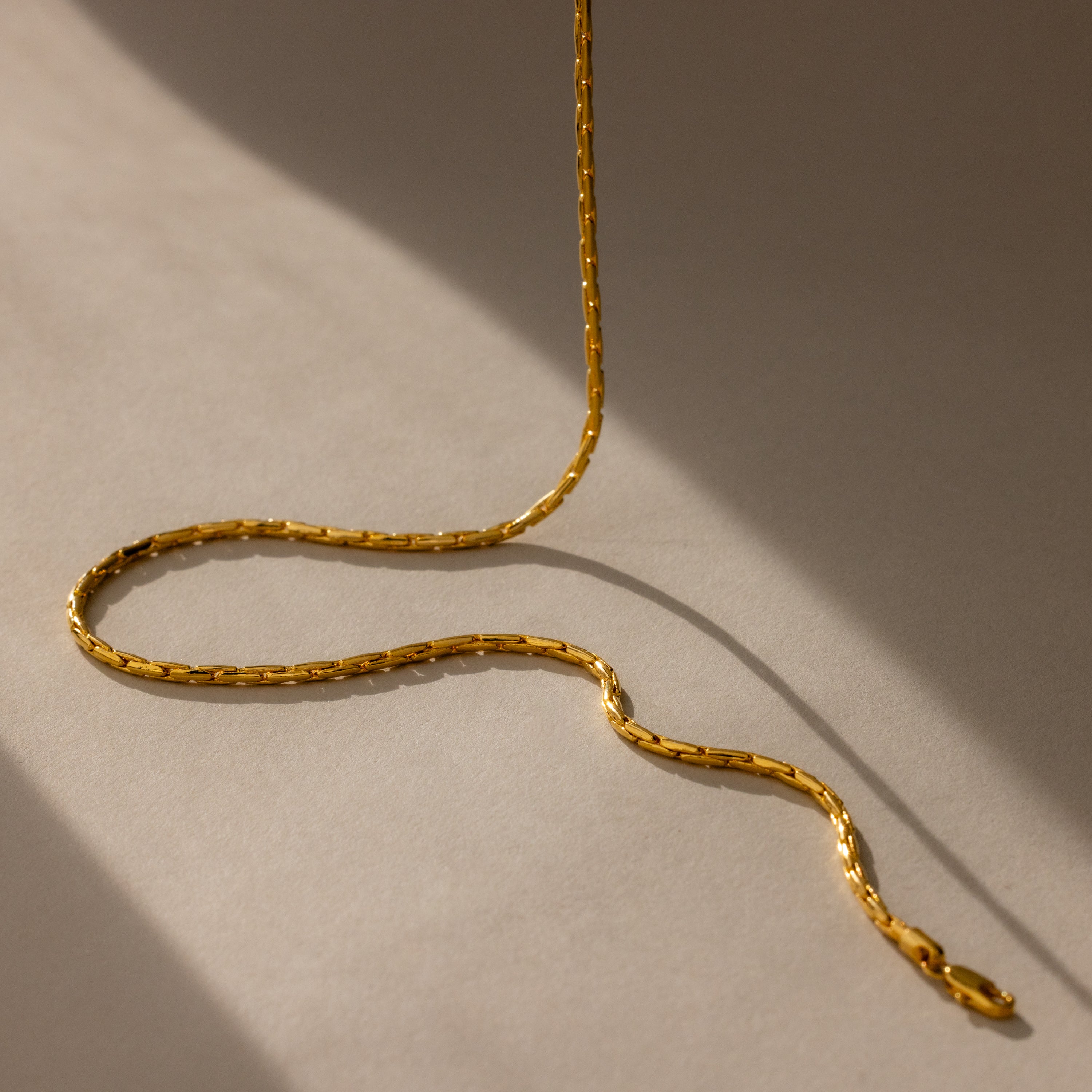 The Bold Link Chain Necklace in 18K Gold rests in gentle curves on a beige surface, casting soft, angled shadows—an eye-catching modern chain made to stand out.