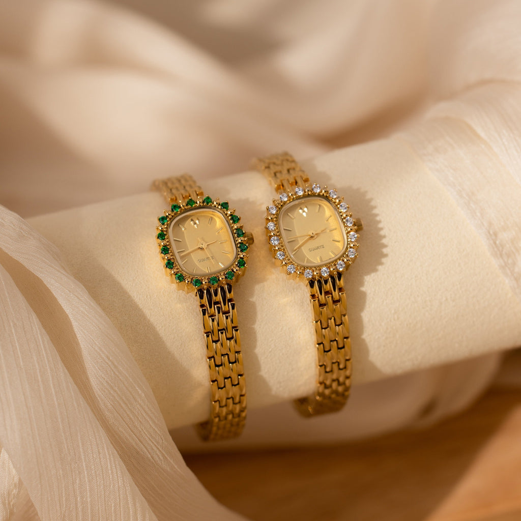 Two elegant Pave Blossom Timepiece watches—one with green CZ gemstones, the other with clear—rest on soft fabric. These jeweled bezels add a touch of luxury to any look.