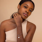 Woman in a one-shoulder top wearing the Round Pearl Charm in Silver bracelet, posing with hand on neck.