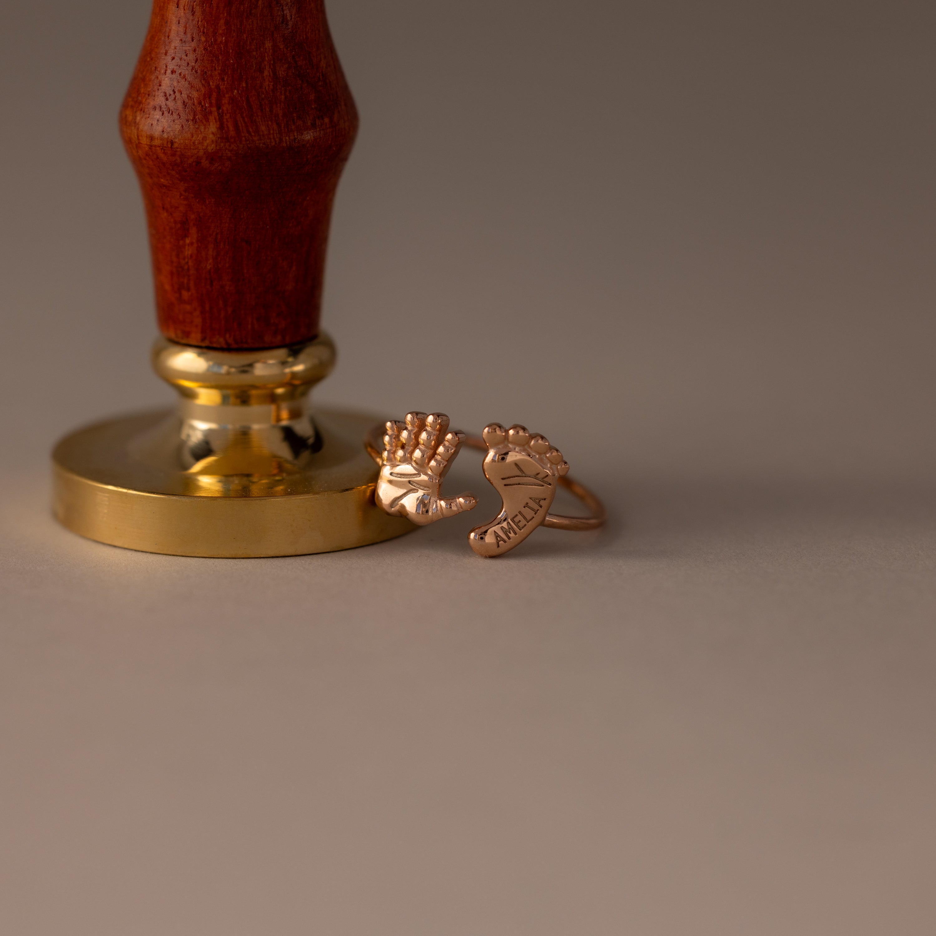 The Hand & Footprint Duo Name Ring in Rose Gold sits on a beige surface—personalized with a hand and footprint plus the name Milen, it’s a perfect keepsake jewelry gift for new parents.