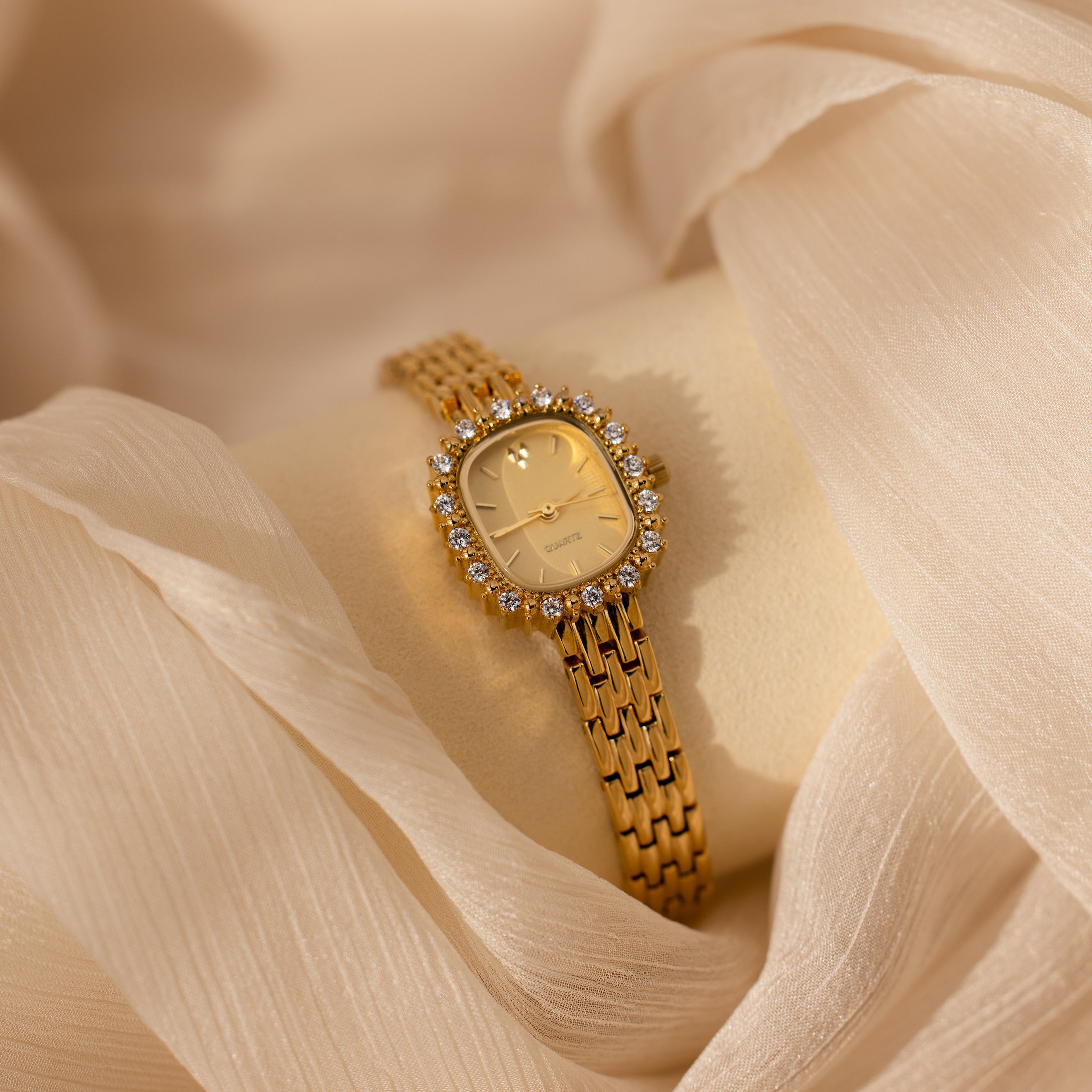 The Pave Blossom Timepiece is an elegant womens watch with a diamond-studded bezel that shines beautifully against a soft beige fabric background.