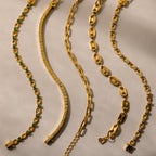 Five gold bracelets with unique designs arranged in wavy lines on a light beige surface—the Corporate Gift Box offers a stunning selection of curated jewelry, ideal for any special occasion.