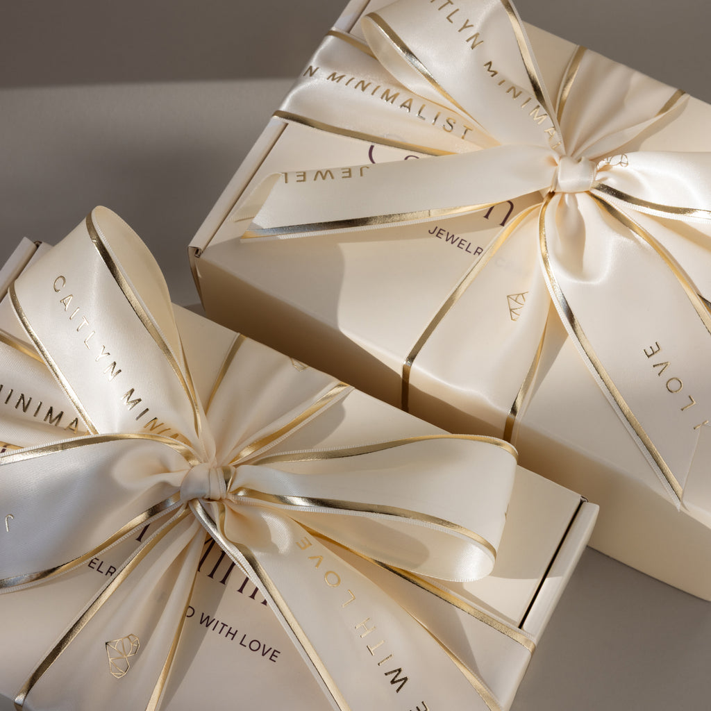 Two Gift Wrap Add-On boxes in cream with shiny ribbons and gold text, stacked on a neutral background, highlight the elegant touch this service brings to your gift.