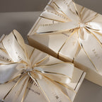 Two Gift Wrap Add-On boxes in cream with shiny ribbons and gold text, stacked on a neutral background, highlight the elegant touch this service brings to your gift.