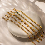 The Bold Mariner Chain Bracelet, adorned with green and clear gemstones, shines on smooth stone under dappled light—ideal for statement jewelry lovers.