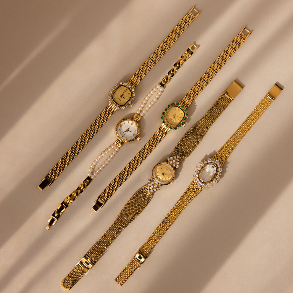 Five vintage gold wristwatches, including the Pave Blossom Timepiece with jeweled details and decorative bands, arranged on a beige surface.
