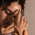A woman with curly hair showcases the Harlow Diamond Ring in Sterling Silver, adorned with delicate marquise diamonds and small gemstones, softly illuminated on her finger.