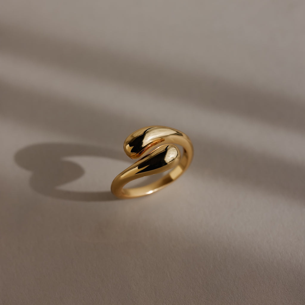 A shiny, gold, modern Duo Dome Ring with an adjustable band casts a shadow on a neutral surface.