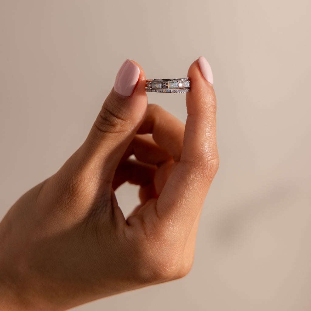 A hand with pink nail polish holds a Pave Opal Ring Set in Sterling Silver, featuring sparkling stones and a timeless design against a neutral background.