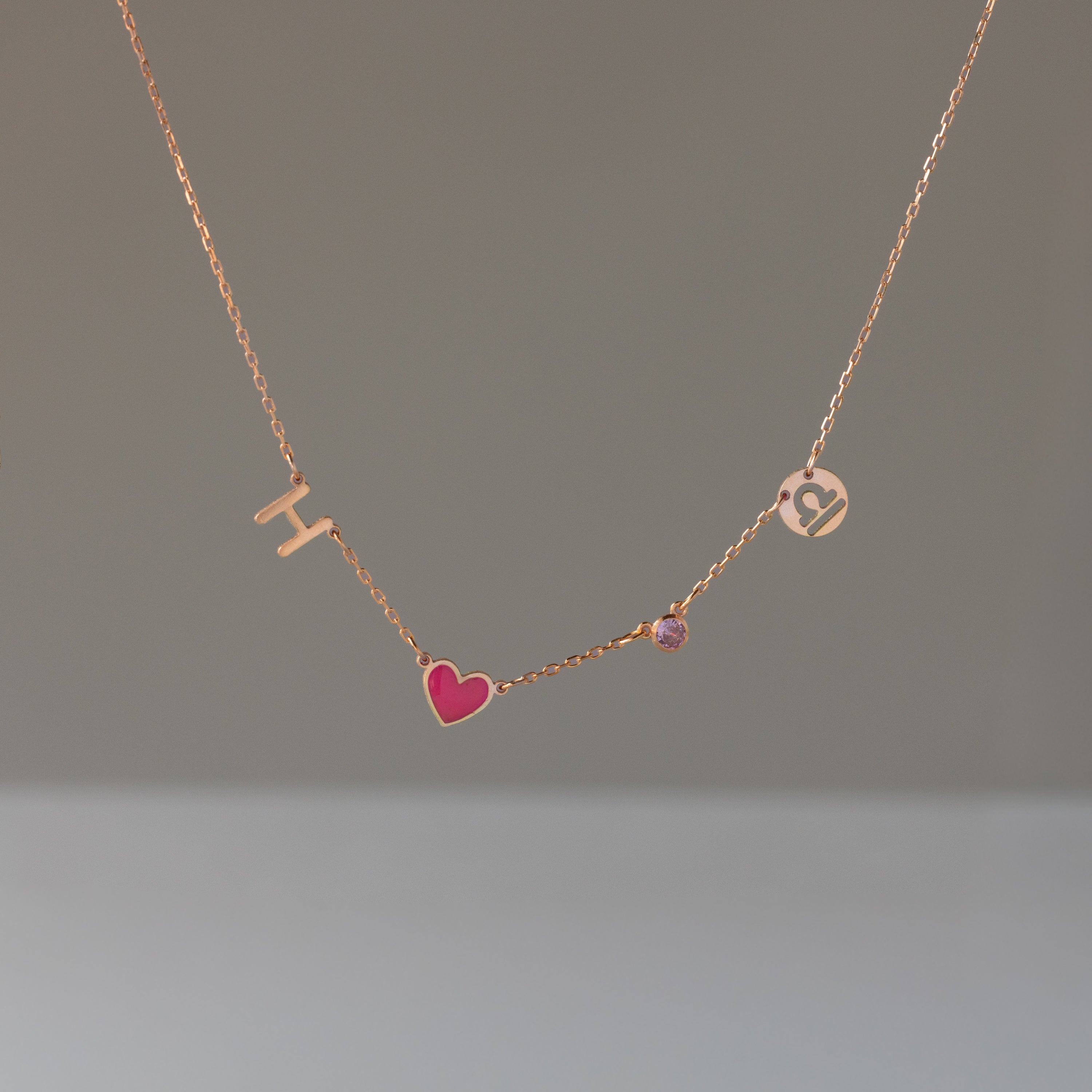 Dainty Space Charm Necklace in Rose Gold featuring gold letters H and J, a pink heart, and a small gem—perfect as a personalized gift for any occasion.