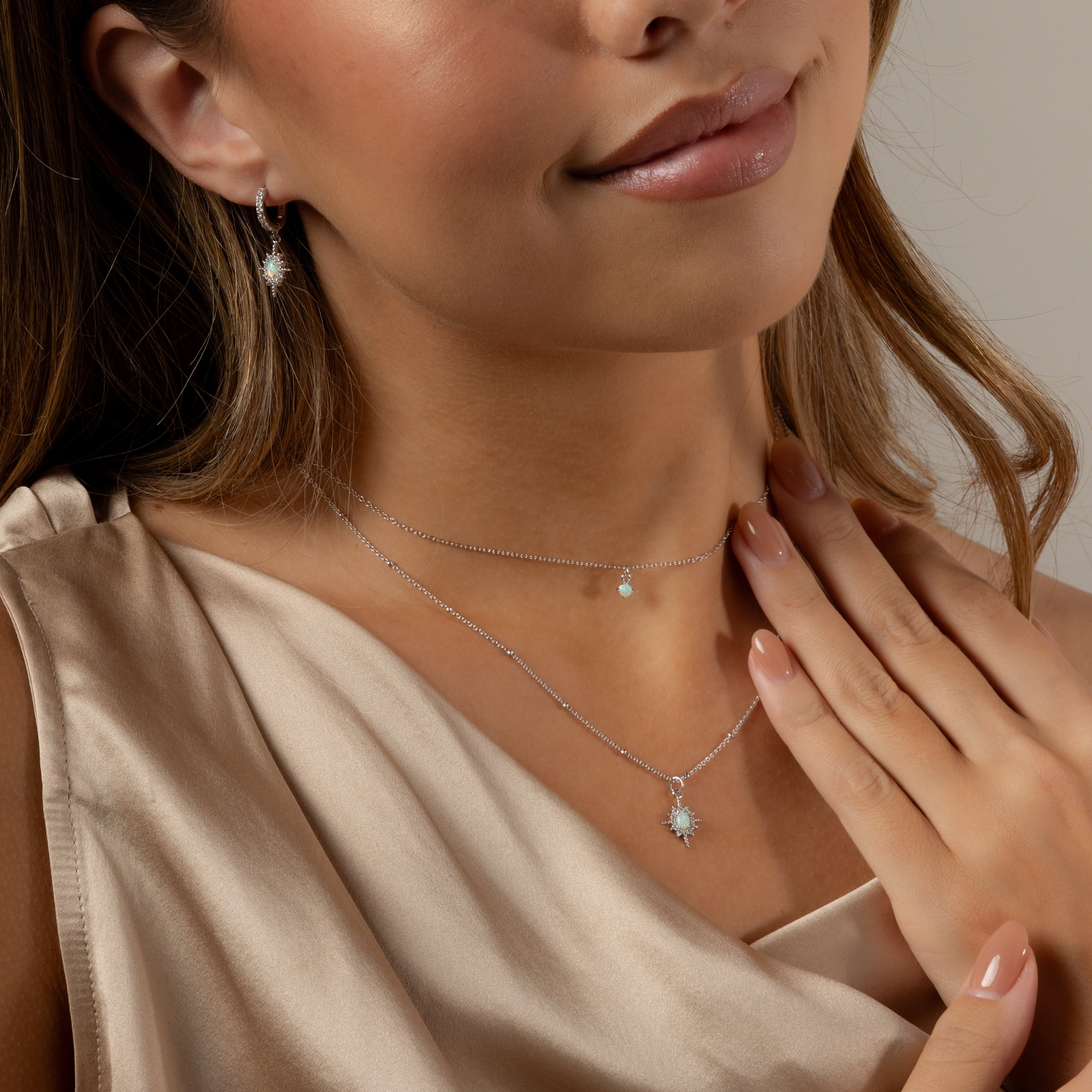Woman wearing a beige satin top and the Opal Star Necklace & Earrings Set in Silver, featuring two delicate silver necklaces with small pendants and matching silver earrings.
