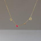 The Dainty Space Charm Necklace features a gold chain with an H charm, pink heart, small pink gem, and a round pendant with a C cutout—perfect for adding customizable elegance to your everyday style.