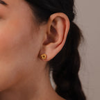 Close-up of a woman's ear wearing Rope Knot Studs, small round gold earrings; her hair is styled in a braid for an elegant, classic look.