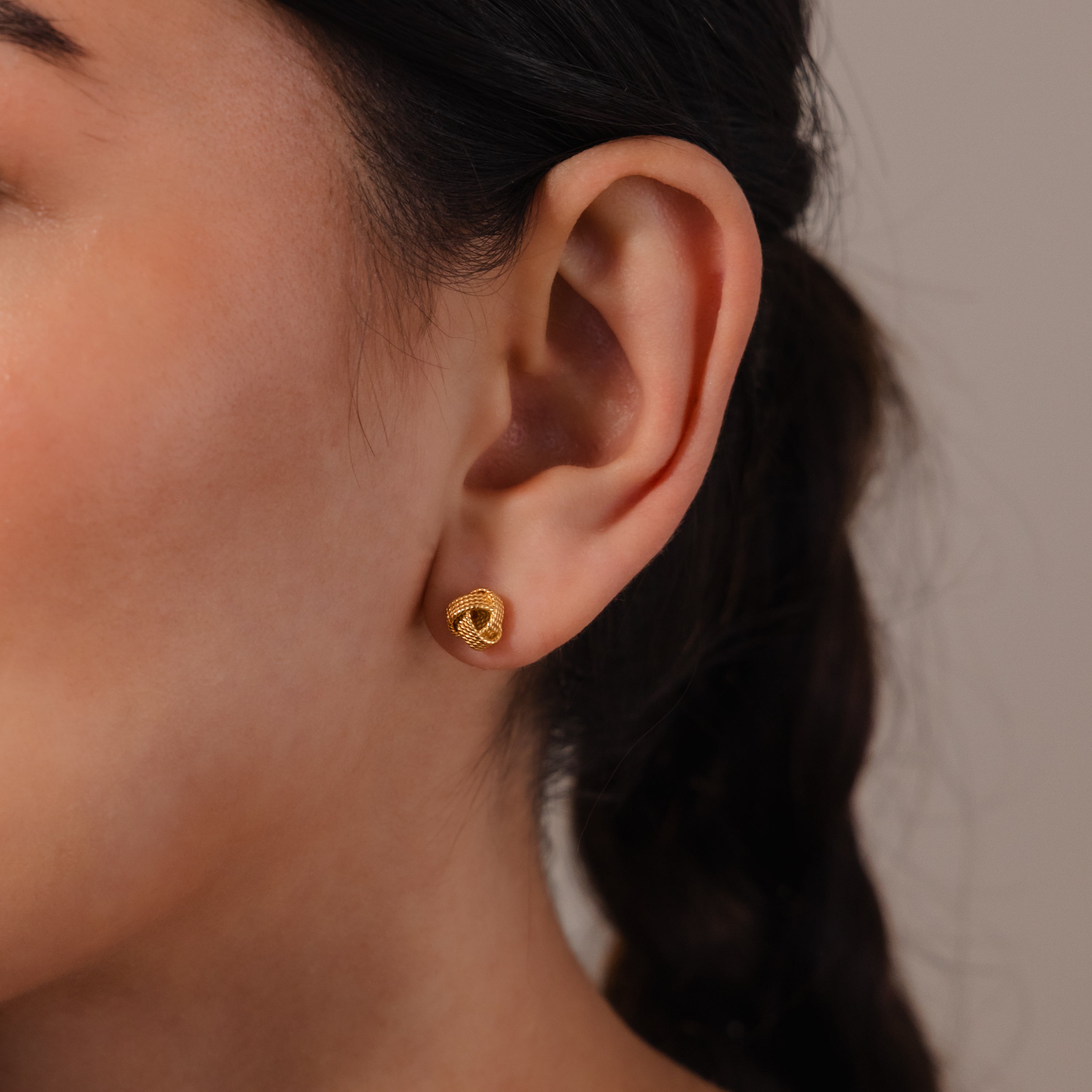 Close-up of a woman's ear adorned with Rope Knot Studs in 18K Gold; her hair is braided at the back.