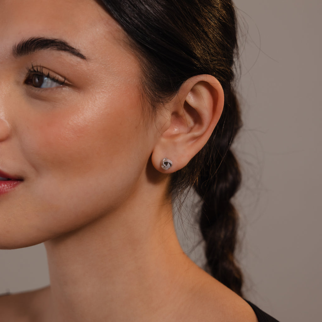 Woman with braided dark hair wears the Rope Knot Studs in Silver—a small, round earring—shown in partial profile against a plain background, perfect for those seeking subtle and elegant jewelry.