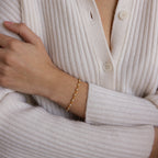 A person in a cream ribbed sweater wears the Eternity Pearl Bracelet in 18K Gold, pairing it with an infinity chain for an elegant jewelry look.