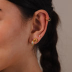 Close-up of an ear wearing Rope Knot Studs in 18K Gold with two gold hoops and a diamond stud, hair styled in a braid.
