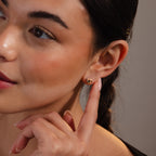 A woman with braided hair smiles softly while pointing to a Rope Knot Stud earring on her ear.