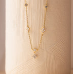 The Ivy Diamond Station Necklace in 18K Gold features small round and star-shaped diamond accents, displayed against a textured beige background.