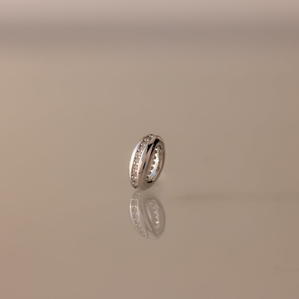 The Pave Dome Charm in Silver glistens with small stones on a smooth, neutral backdrop.