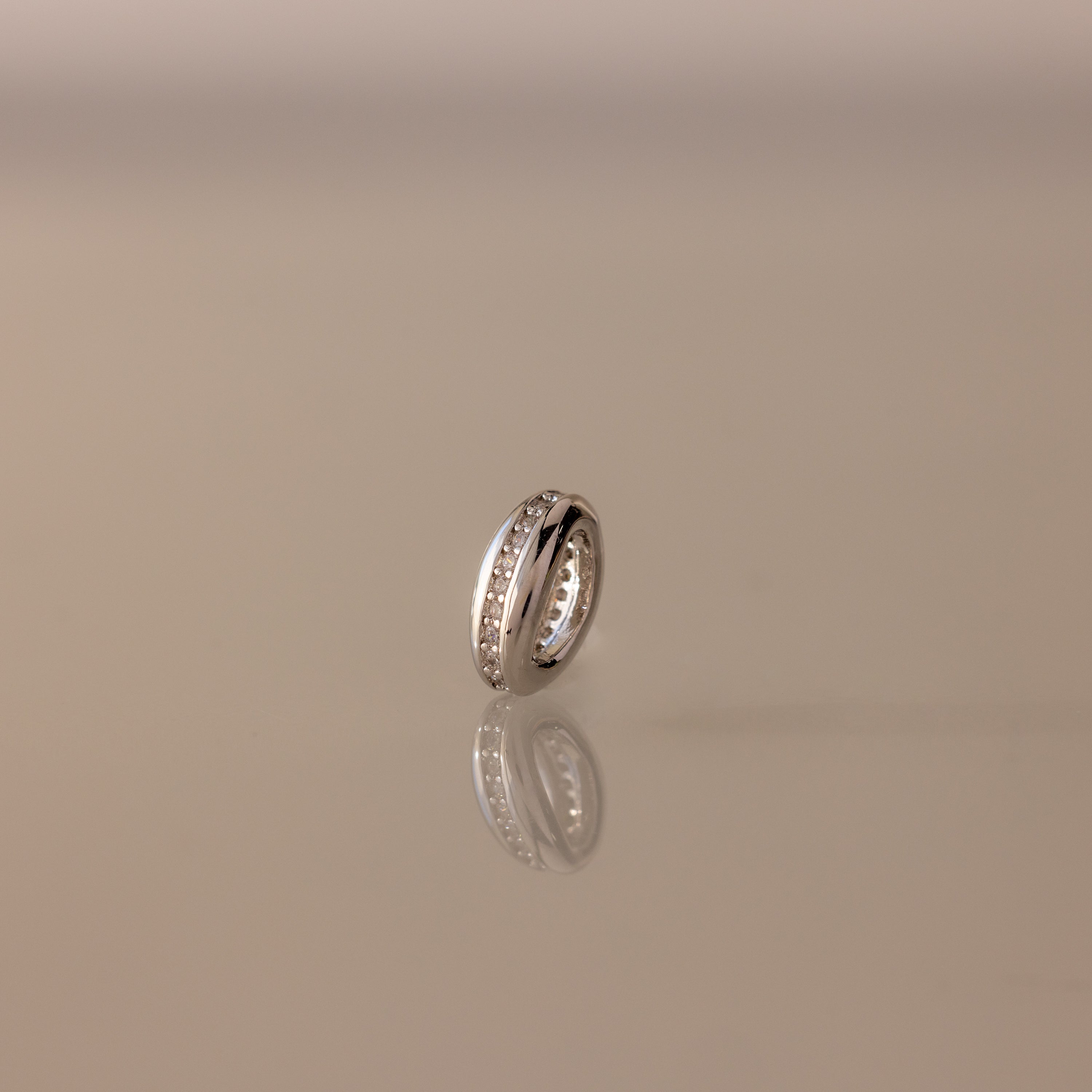 The Pave Dome Charm in Silver glistens with small stones on a smooth, neutral backdrop.